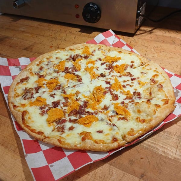 A FYRE PIZZA Co. buffalo chicken and bacon pizza on red and white checkered paper.
