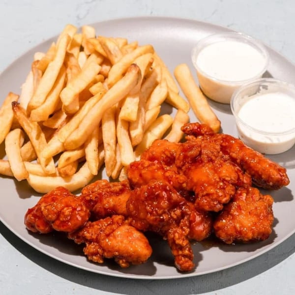 A plate of crispy french fries, saucy boneless wings, and two containers of dipping sauce.