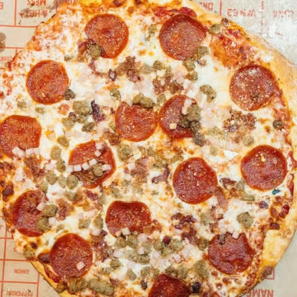 A close-up of a FYRE PIZZA Co. pizza, topped with pepperoni, sausage, and onions.