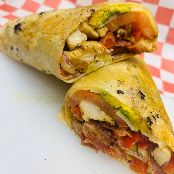 Two halves of a chicken, bacon, avocado, and tomato wrap on a white and red checkered background.