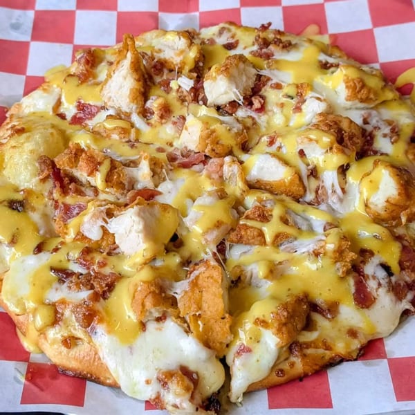 A FYRE PIZZA Co. pizza with fried chicken, bacon, and cheese sauce on checkered paper.