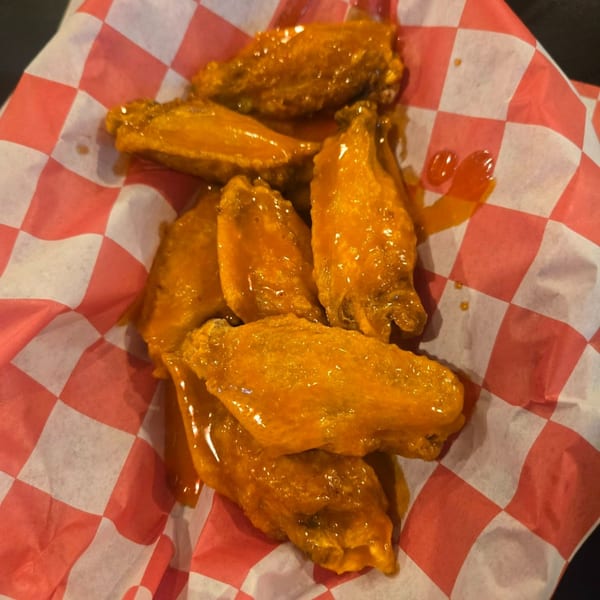 A close-up of several golden-brown chicken wings coated in a glossy sauce, served on red and white checkered paper.