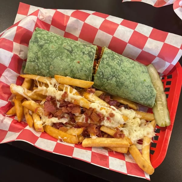 A green wrap, loaded fries with melted cheese and bacon, and a pickle spear in a red basket.